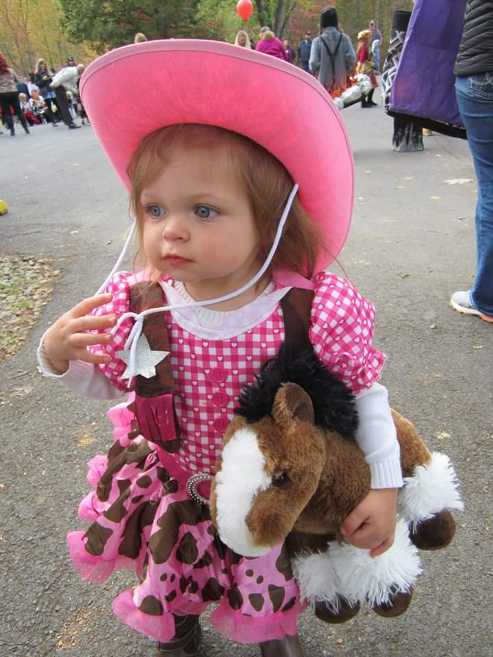 little girl dressed up as a pink cowgirl holding a stuffed horse